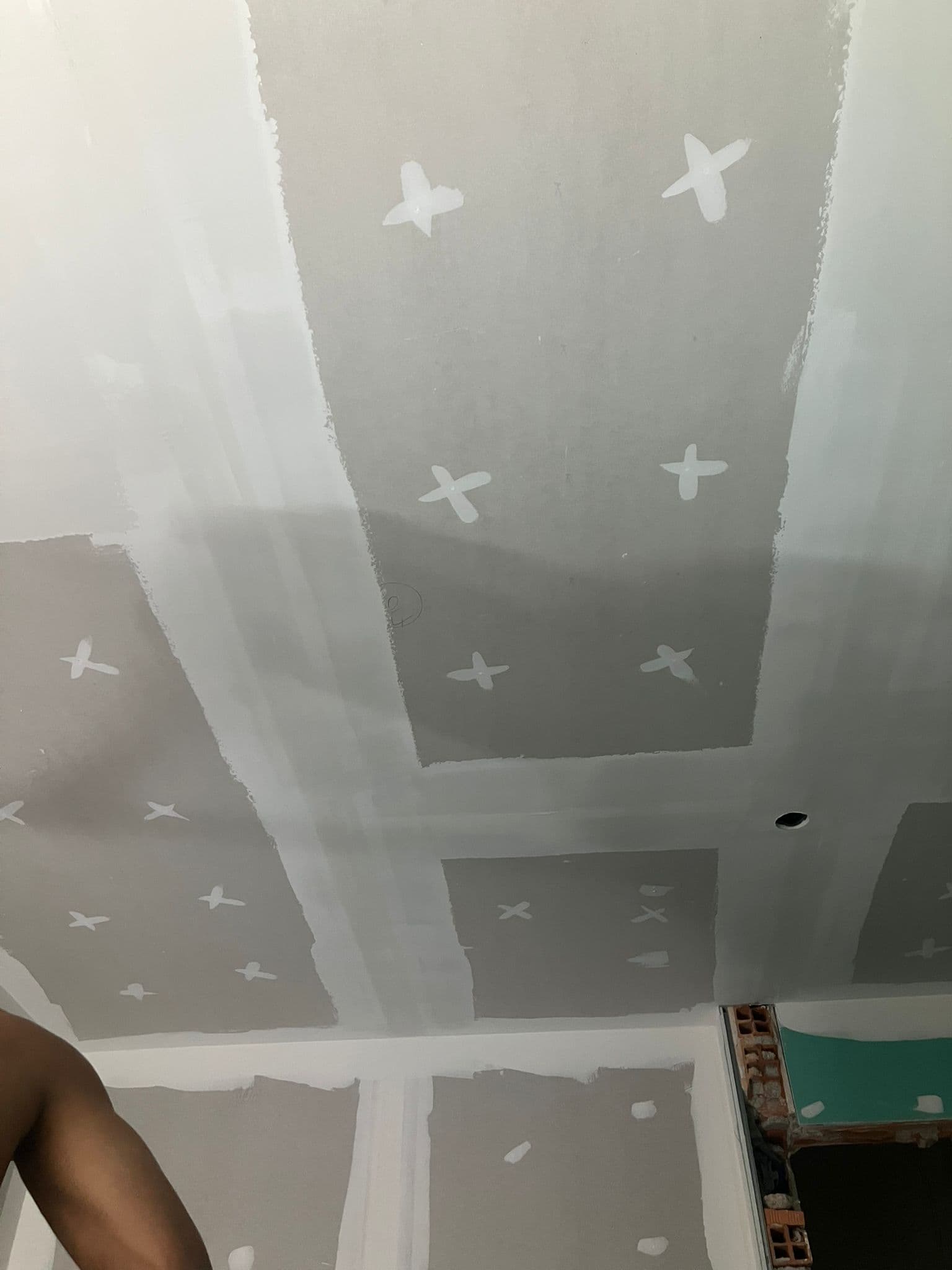 Teto de drywall com massa branca cobrindo juntas e parafusos em formato de pequenas cruzes.